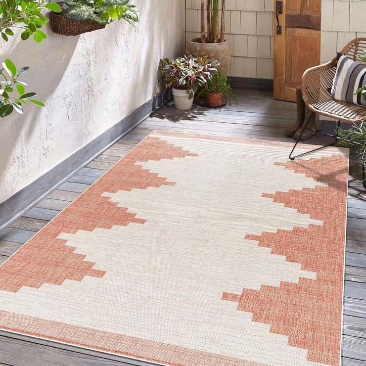 Hauteloom Djugun Peach Fuzz indoor/outdoor rug with Aztec geometric pattern on a wooden patio, surrounded by potted plants