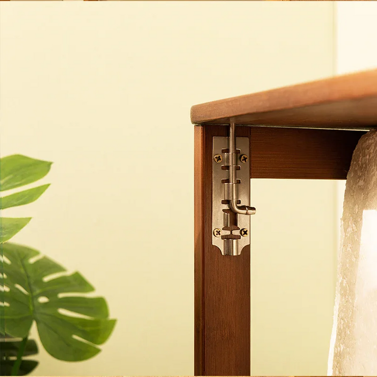 Close-up of the metal bolt latch mechanism on a brown bamboo folding desk leg, with a plant in the background.