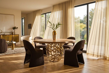 Acacia live edge dining table with an openwork brass-finished pedestal, surrounded by four dark upholstered chairs in a sunlit dining room.