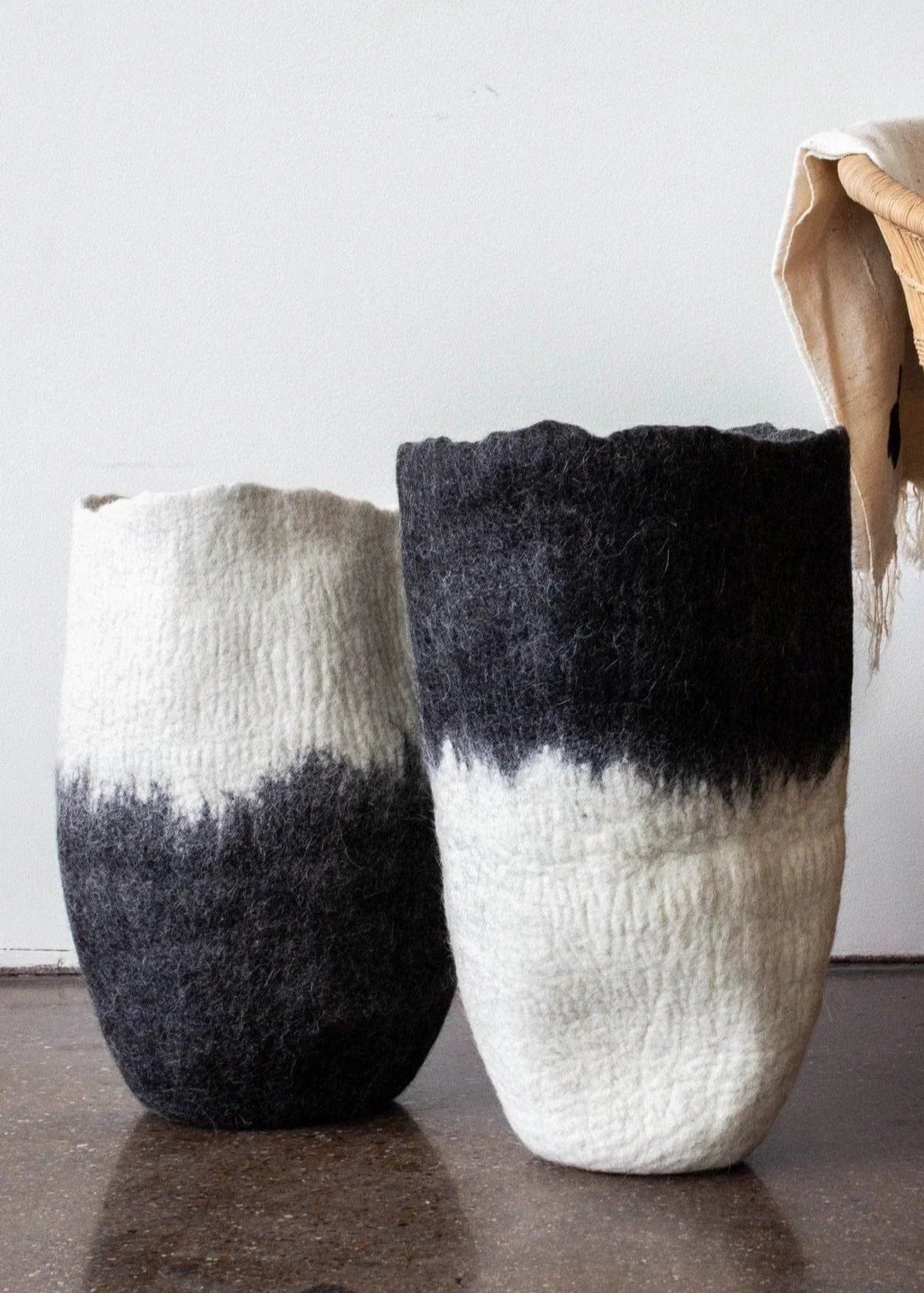 Two black and white ombré felted wool floor vases side by side showing contrasting colorways on dark concrete floor with dried botanical stems


