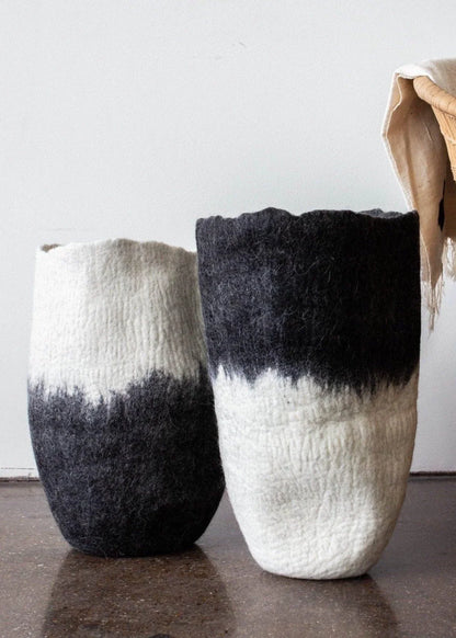 Two black and white ombré felted wool floor vases side by side showing contrasting colorways on dark concrete floor with dried botanical stems

