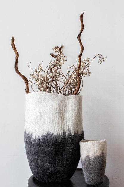 Large white to charcoal ombré felted wool floor vase styled with dried branches and wildflowers on black pedestal against white wall

