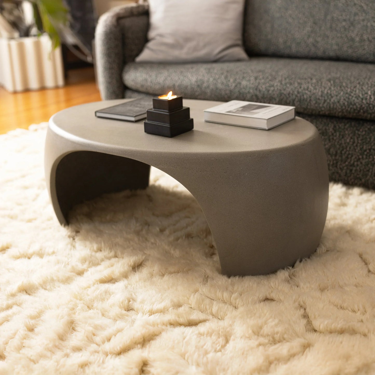 Slate Micro Terrazzo Nook concrete coffee table styled with tiered candle holder and art books on ivory shag rug beside charcoal sofa

