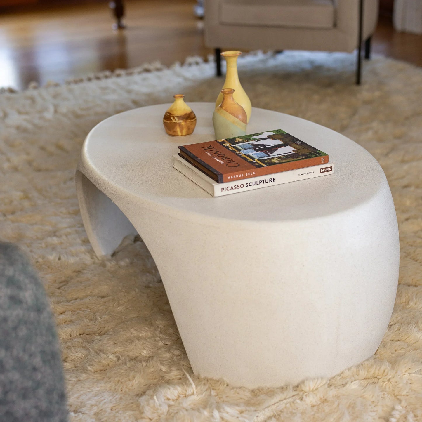 White Micro Terrazzo Nook concrete coffee table styled with gold vases and art books on ivory shag rug

