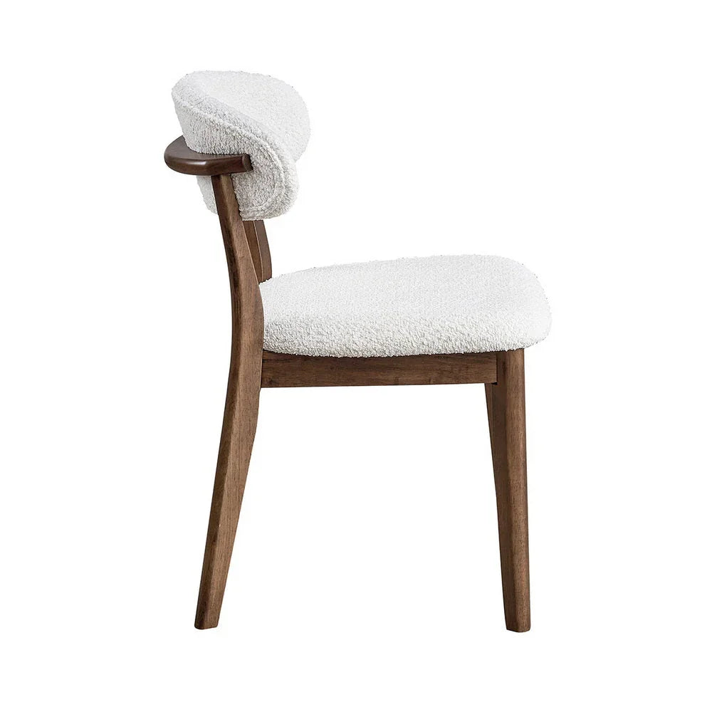 Walnut Scandinavian dining chair with bouclé upholstered seat and curved backrest shown from side on white studio background

