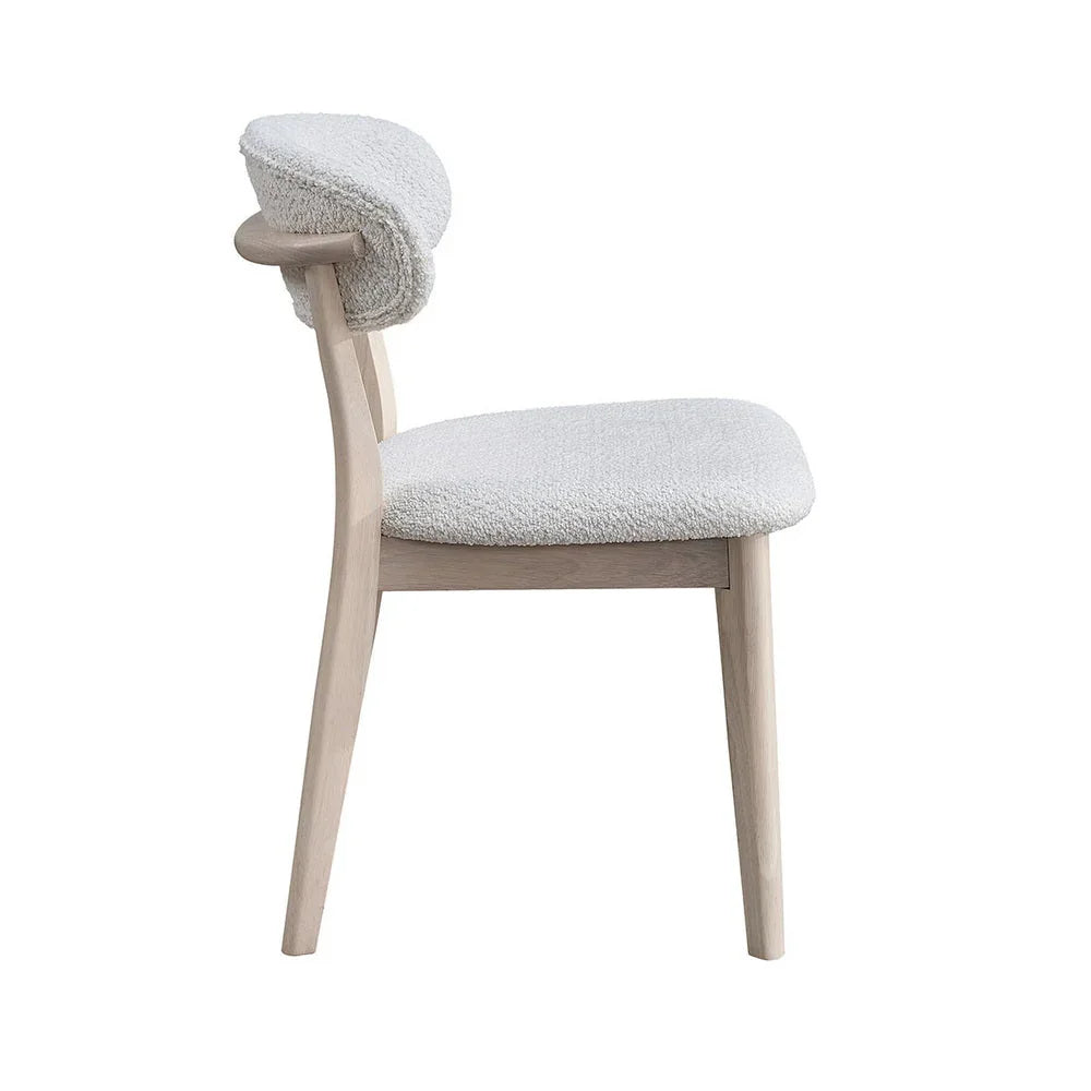 White-washed Scandinavian dining chair with bouclé upholstered seat and curved backrest shown from side on white studio background

