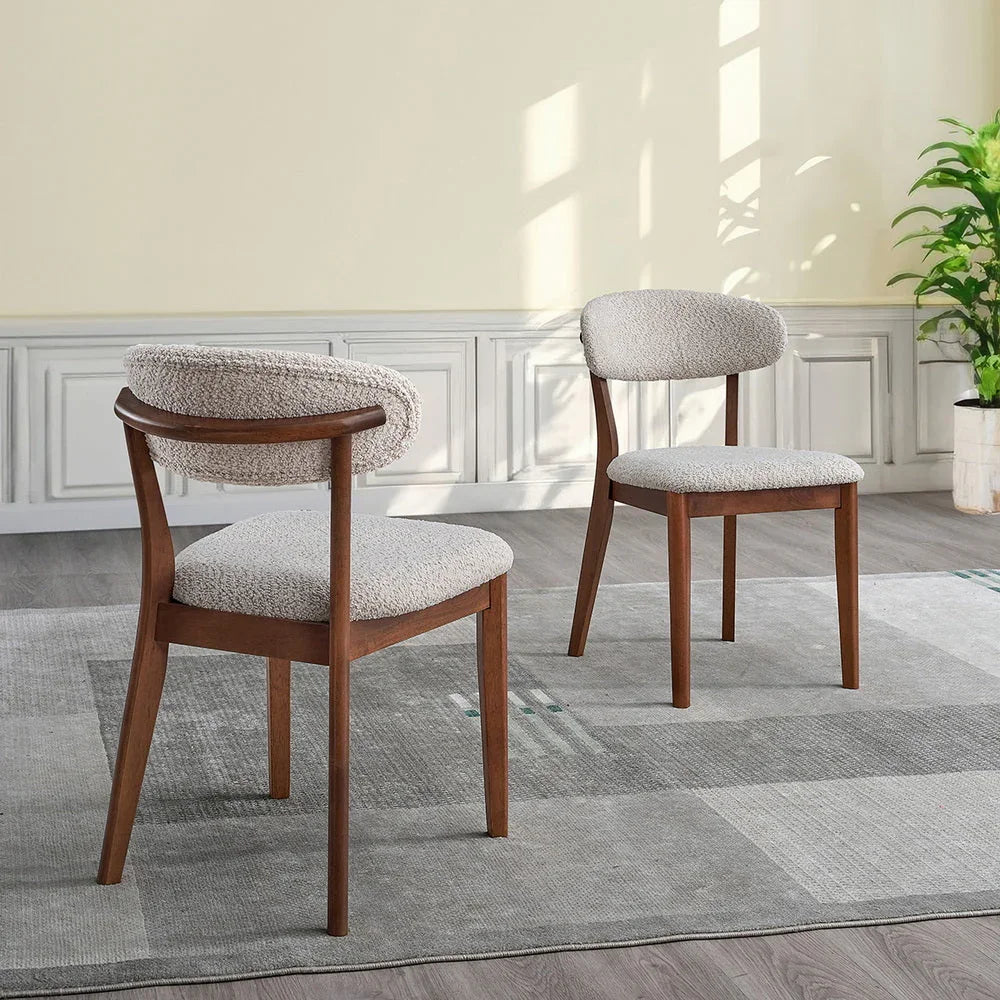 Two cherry Scandinavian dining chairs with bouclé upholstered seats and curved backrests styled in a bright room with gray area rug and indoor plant

