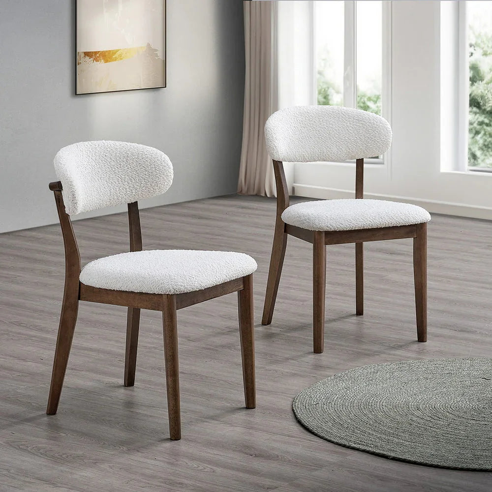 Two walnut Scandinavian dining chairs with bouclé upholstered seats and curved backrests styled on light wood floor beside round woven rug

