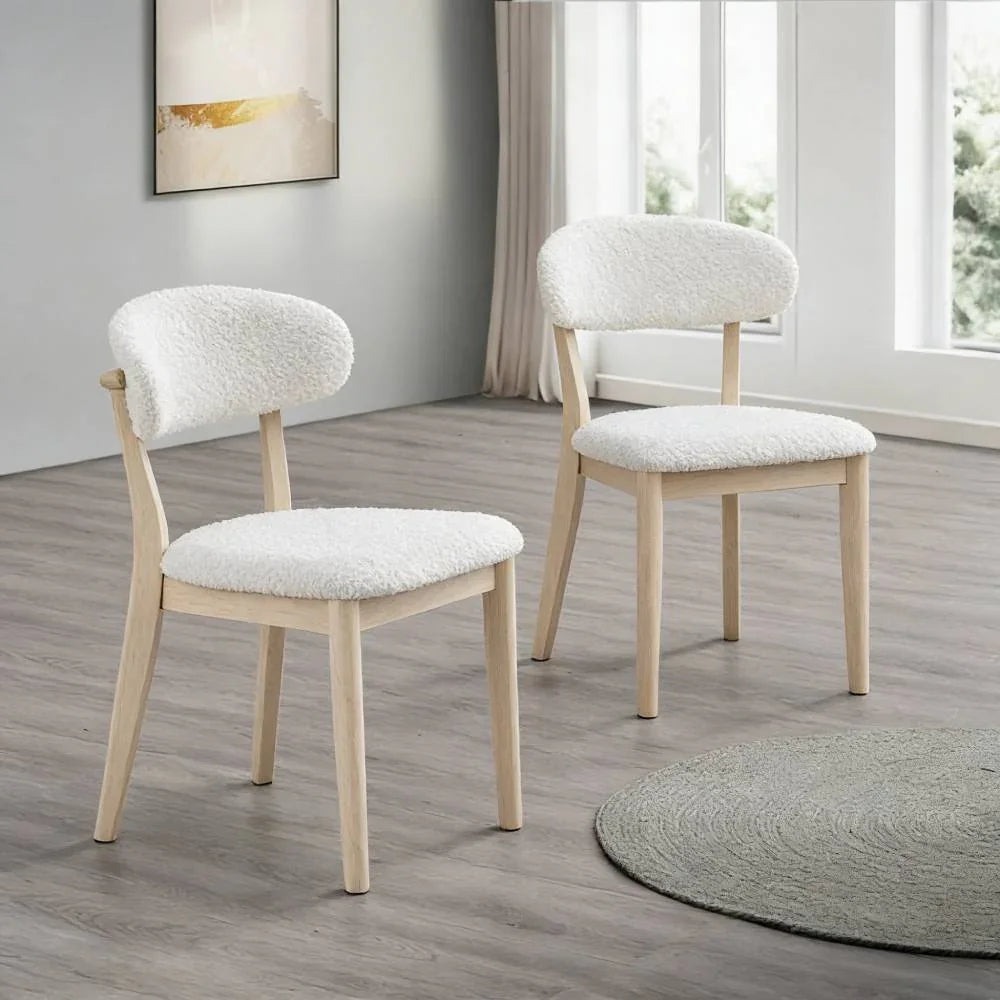 Two white-washed Scandinavian dining chairs with bouclé upholstered seats and curved backrests styled on light wood floor beside a round woven rug

