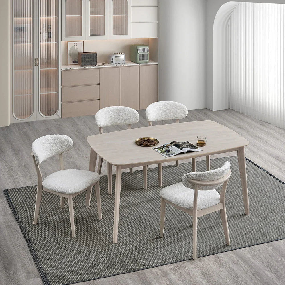 White-washed Scandinavian wood dining set with four upholstered bouclé chairs styled in a modern open-plan kitchen with light wood floors and gray rug

