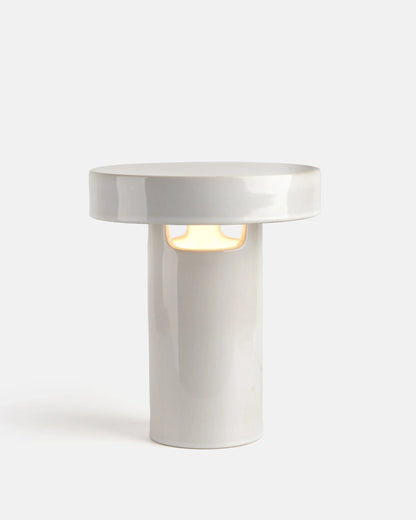 White glossy cylindrical ceramic table lamp with slot opening casting warm light on white background

