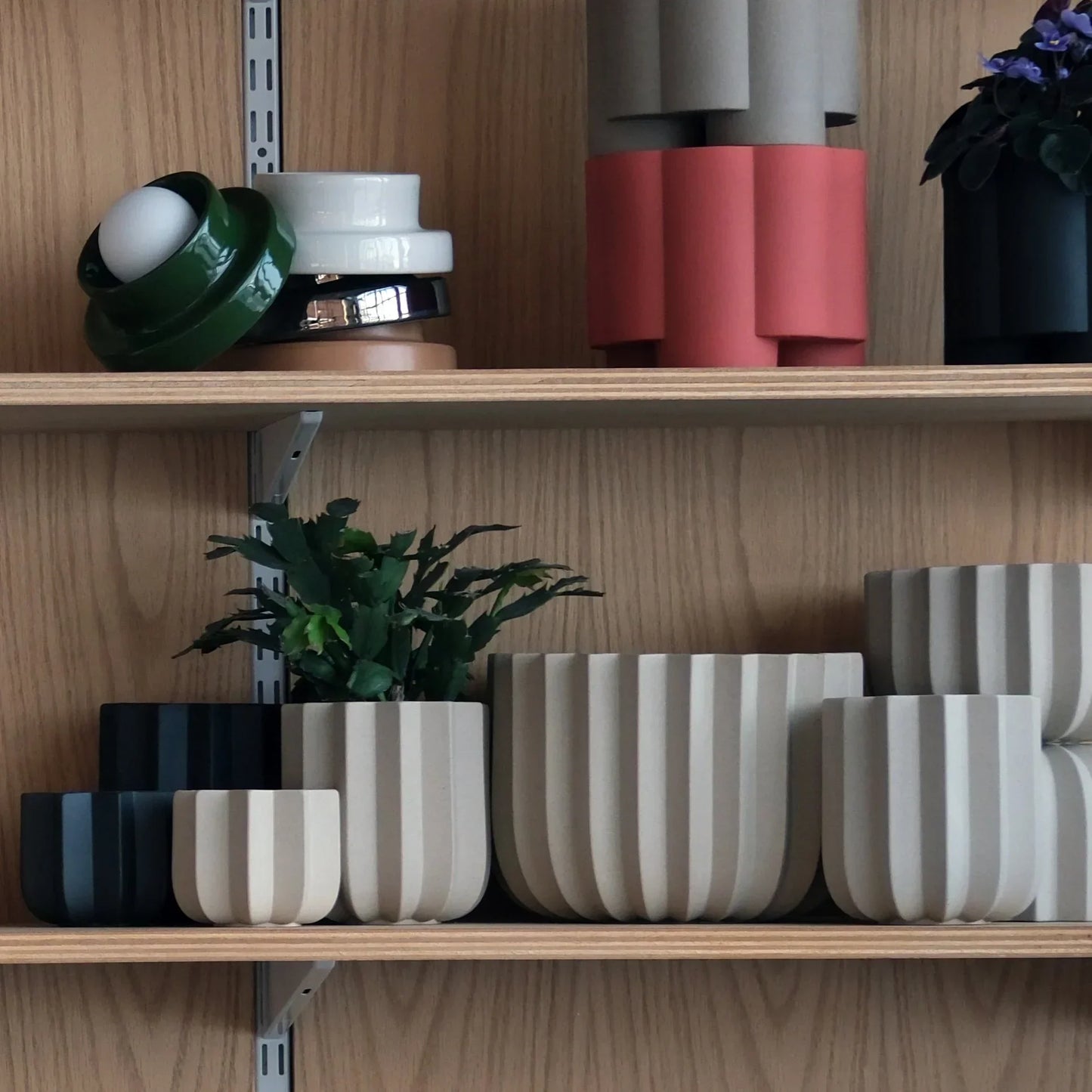 Wrap Planter collection in dune and black displayed in multiple sizes on oak studio shelf with green plant and ceramic objects

