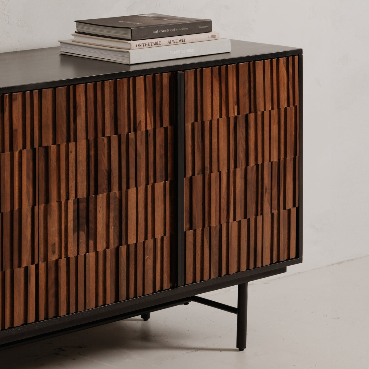 Close-up of the solid sheesham and mango wood sideboard showing textured brown doors, a slim dark handle, and the black iron base, with books on top. 