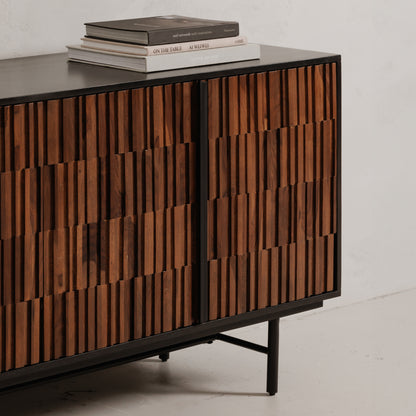 Close-up of the solid sheesham and mango wood sideboard showing textured brown doors, a slim dark handle, and the black iron base, with books on top. 