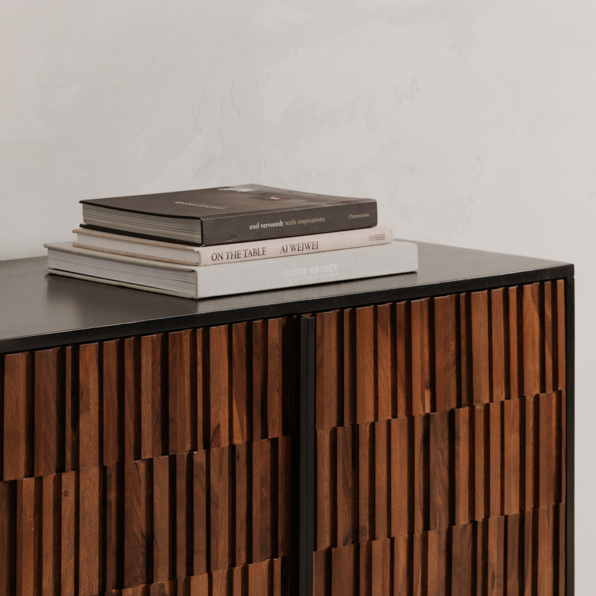 Close-up of the solid sheesham and mango wood sideboard with books on its dark tabletop, showing textured brown doors and a slim dark handle. 