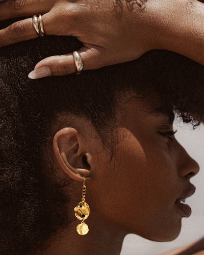 Woman wearing gold vermeil sapphire coin drop earrings styled with stacked silver rings in a luxury editorial portrait
