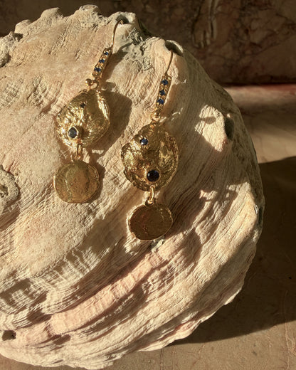 Gold vermeil sapphire coin drop earrings resting on natural stone surface with warm artisan light detail