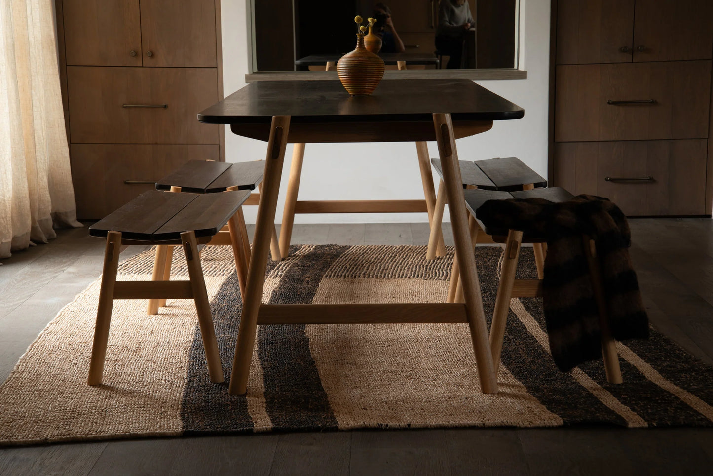 Handwoven rectangular sisal rug tea black stripe variant styled under dining table and benches in warm moody dining room setting