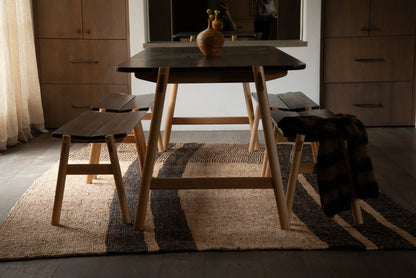 Handwoven rectangular sisal rug tea black stripe variant styled under dining table and benches in warm moody dining room setting