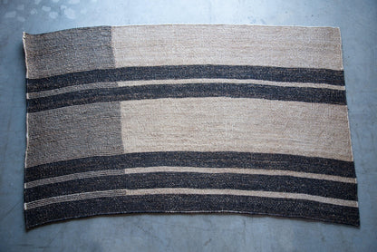 Full flat lay of handwoven rectangular sisal rug tea black variant showing asymmetric block stripe pattern cream field charcoal stripes

