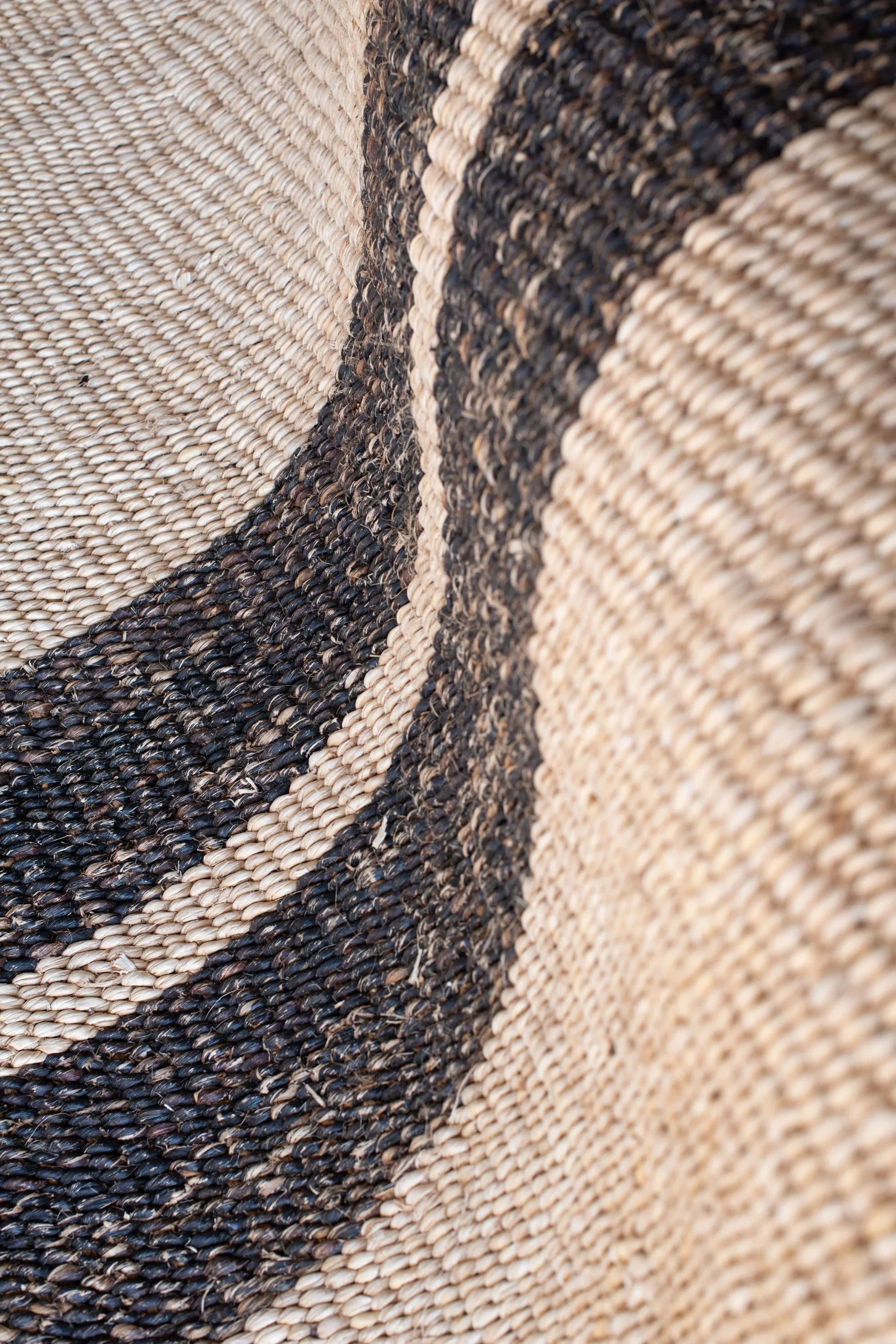 Close-up of handwoven sisal rug tea black variant showing stripe transition natural cream fiber meeting charcoal black weave