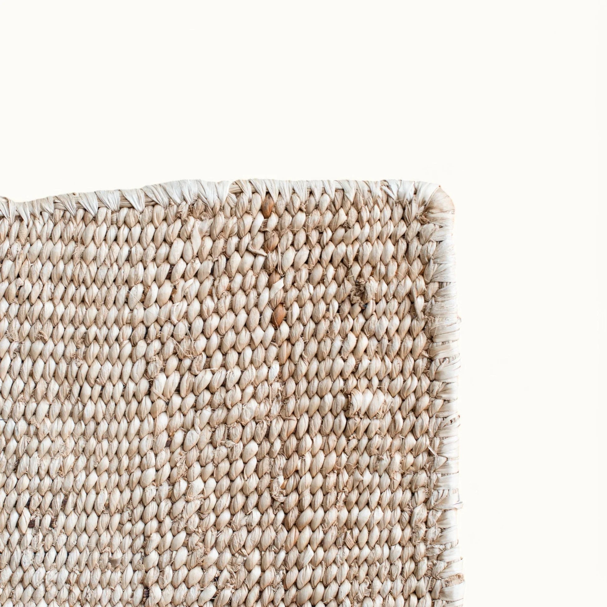 Corner edge detail of handwoven sisal rug tea variant showing natural cream weave surface raw fringe edge finishing and fiber texture