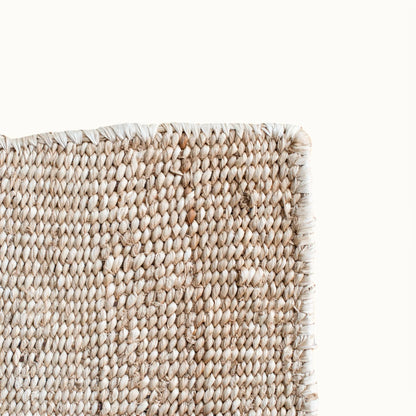 Corner edge detail of handwoven sisal rug tea variant showing natural cream weave surface raw fringe edge finishing and fiber texture