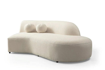 Ivory boucle left facing chaise sectional with sculptural curved back, two round toss pillows, and armless flowing silhouette on a white background