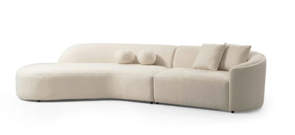 Ivory boucle sculptural curved modular sectional with left facing chaise and toss pillows on a white background