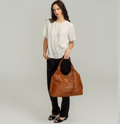 Lady Bird Tote Cuoi lifestyle shot woman hand carry natural leather tote full length side view brass o-ring tassel grey background

