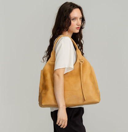 Lady Bird Tote Dijon lifestyle shot woman carrying natural leather tote on shoulder brass o-ring tassel detail grey background

