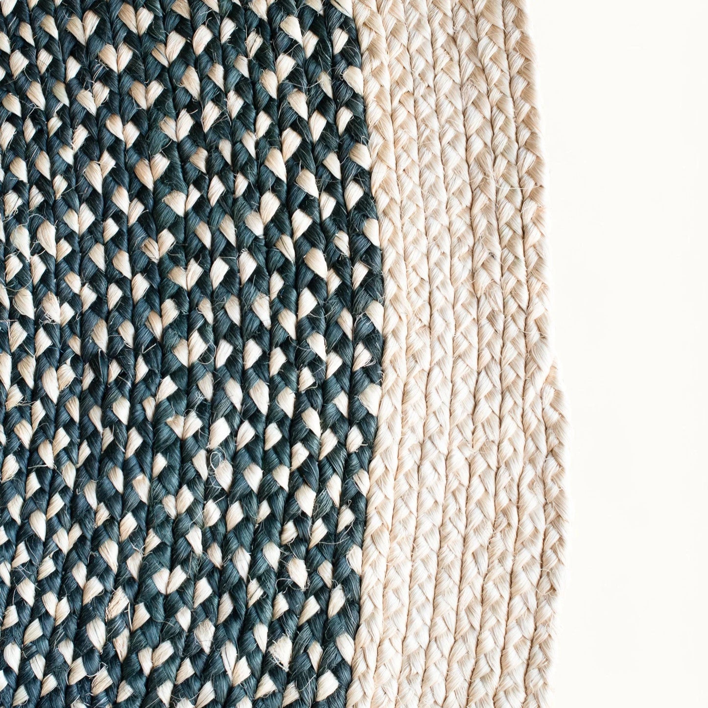 Close-up fiber detail of round sisal rug showing two-tone braid transition between charcoal black and natural cream sisal fiber bundles with visible hand-woven weave structure