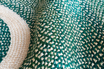 Angled close-up of round sisal rug forest green variant showing curved concentric braid rings with deep teal green and natural cream two-tone weave pattern and individual sisal fiber texture throughout