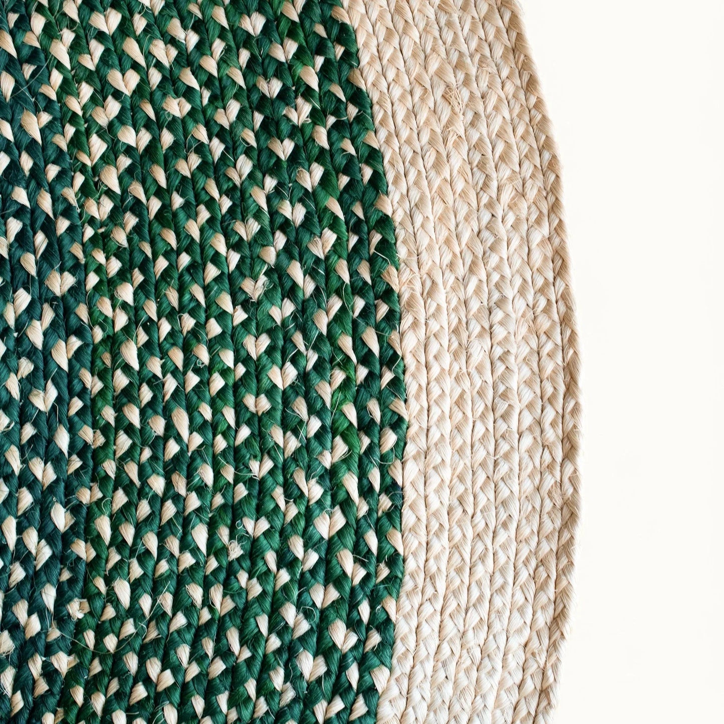 Close-up fiber detail of round sisal rug forest green variant showing two-tone braid transition between deep forest green and natural cream sisal fiber bundles with curved border edge visible