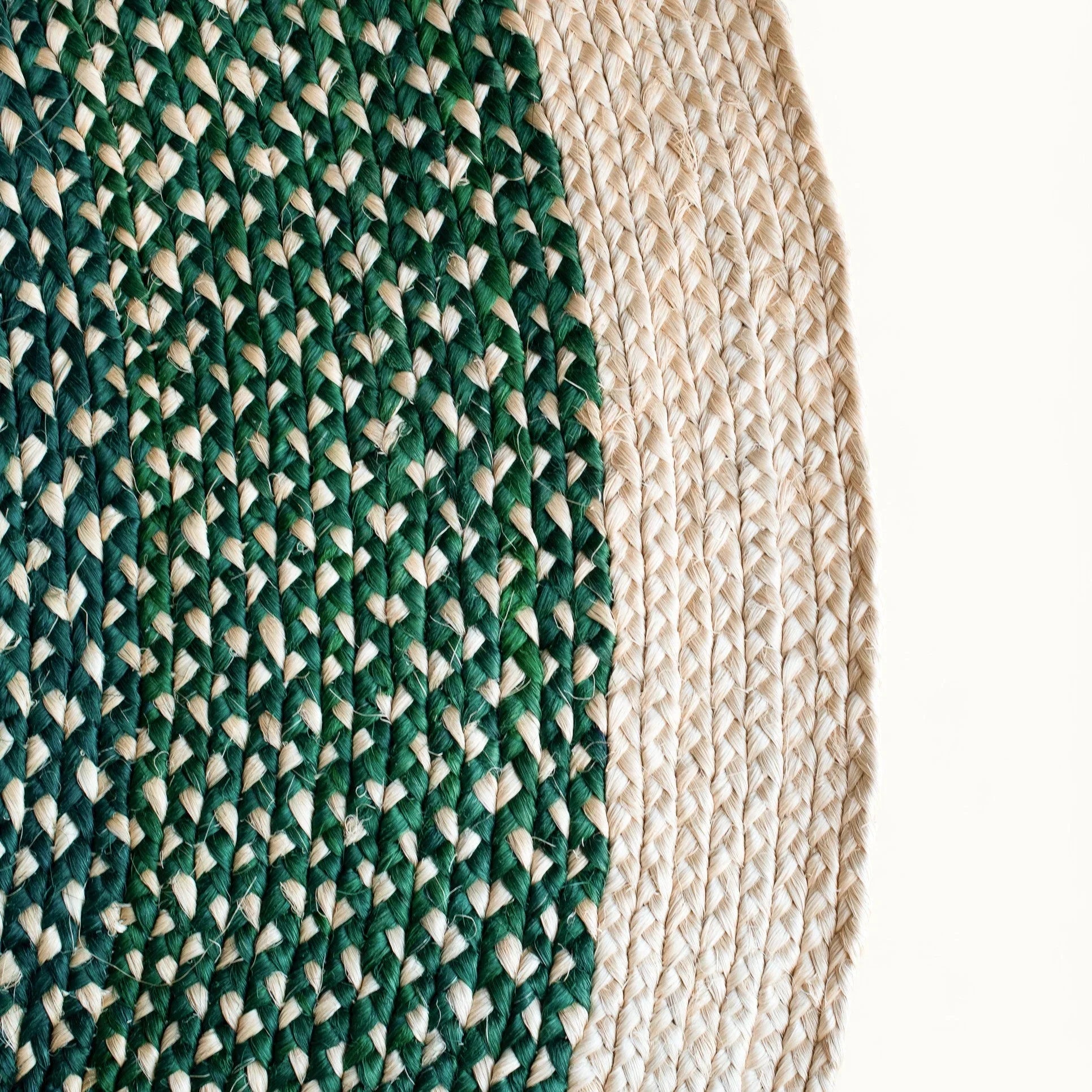 Close-up fiber detail of round sisal rug forest green variant showing two-tone braid transition between deep forest green and natural cream sisal fiber bundles with curved border edge visible