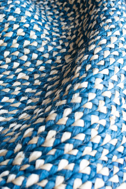 Angled close-up of round sisal rug marine blue variant showing curved concentric braid rings with deep marine blue and natural cream two-tone weave pattern and individual sisal fiber texture throughout