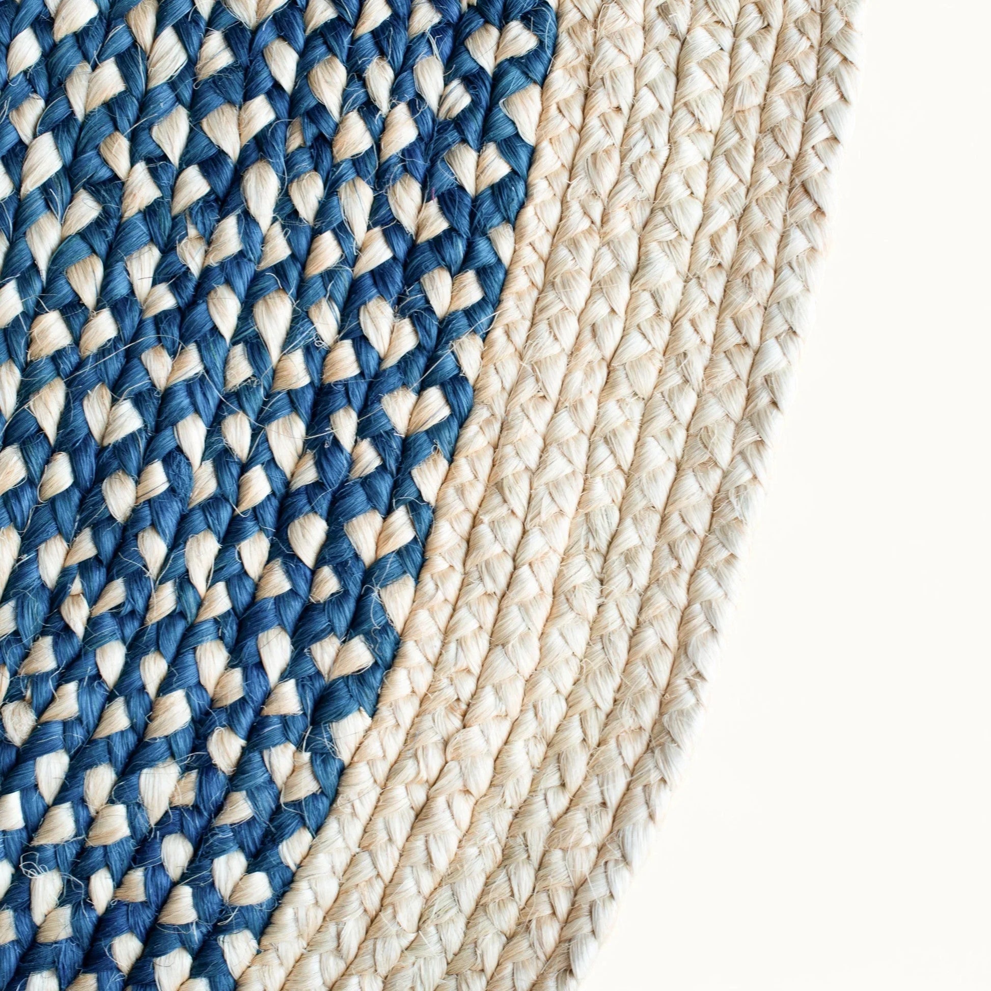 Close-up fiber detail of round sisal rug marine blue variant showing two-tone braid transition between deep marine blue and natural cream sisal fiber bundles with curved border edge on white background