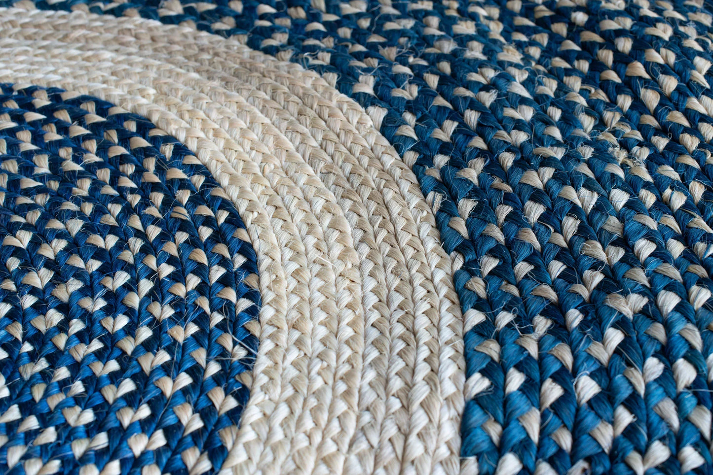 Overhead detail of round sisal rug marine blue variant showing curved cream ring motif separating deep marine blue two-tone braided fields with individual sisal fiber texture throughout
