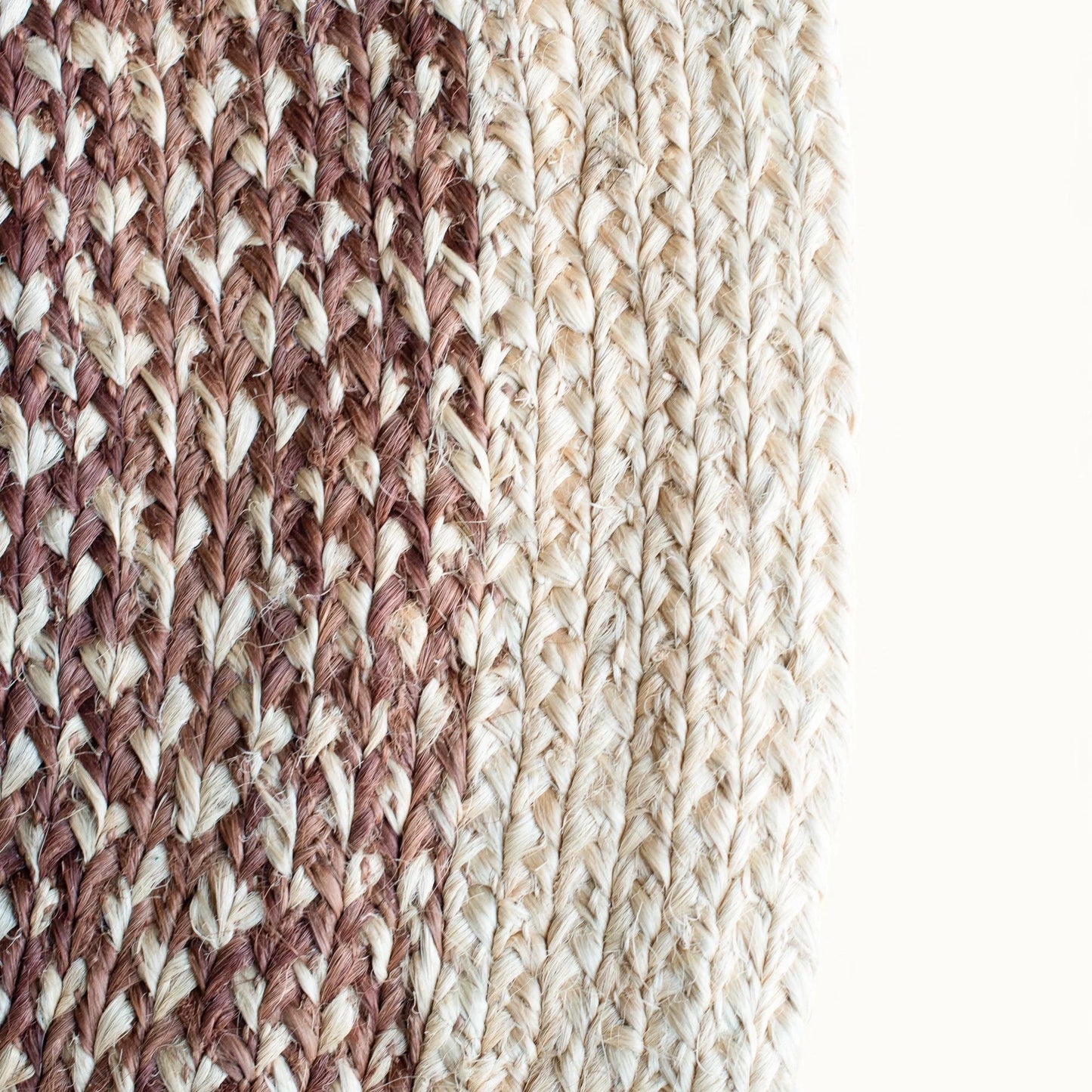 Close-up fiber detail of round sisal rug red earth variant showing two-tone braid transition between dusty mauve rose and natural cream sisal fiber bundles on white background