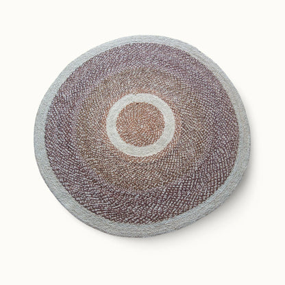 Handwoven round sisal rug red earth variant with warm taupe mauve braided field cream circle ring motif and light grey border on white background