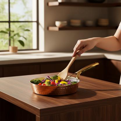 Copper frying pan with brass handle, filled with colorful vegetables, being stirred by a woman's hand in a sunlit kitchen.