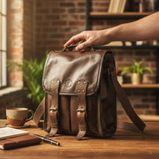 Timeless Brown Bovine Leather Satchel Bag on desk with creative executive's hand, coffee, notebook, pen, & office backdrop.