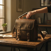 Timeless Brown Bovine Leather Satchel Bag (medium), with a woman's hand reaching inside, on a rustic workbench.