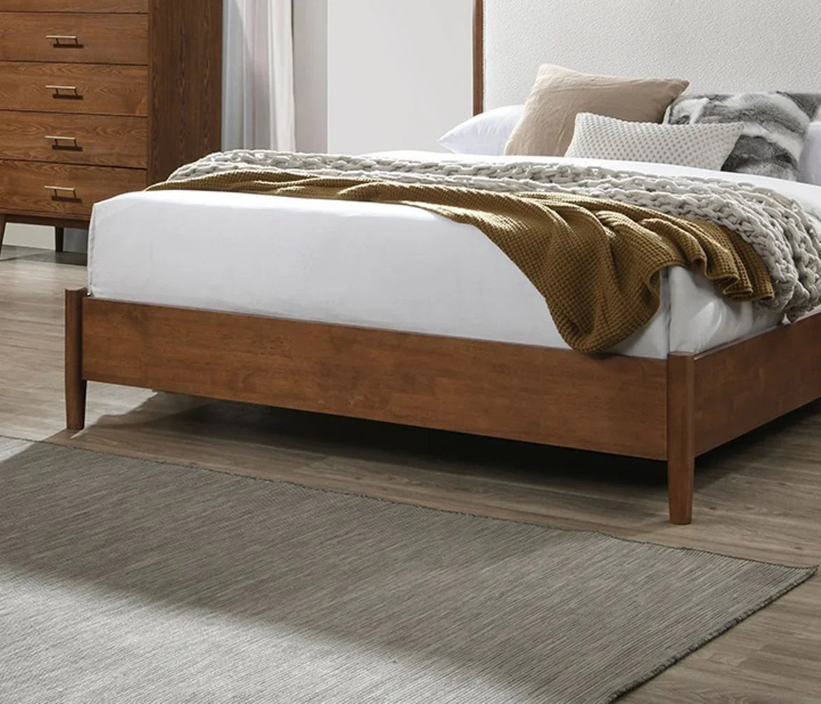 Close-up profile of a low-profile designer bed frame with a textured beige boucle headboard, layered accent pillows, and an elegant walnut finish side rail
