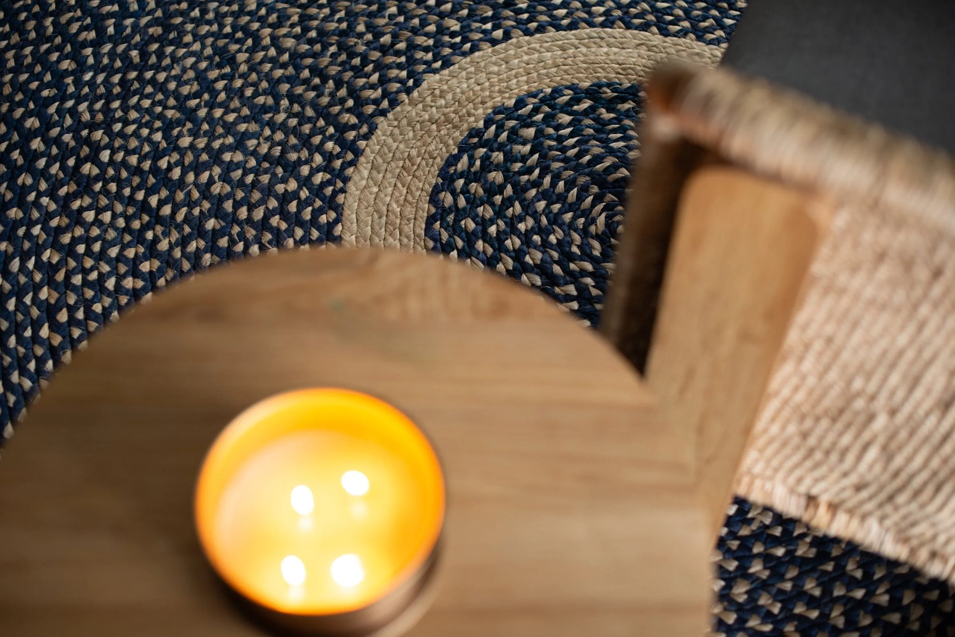Overhead lifestyle detail of medium round sisal rug marine blue variant showing cream ring motif and deep marine blue braided field with round wood coffee table and glowing amber candle bowl in foreground