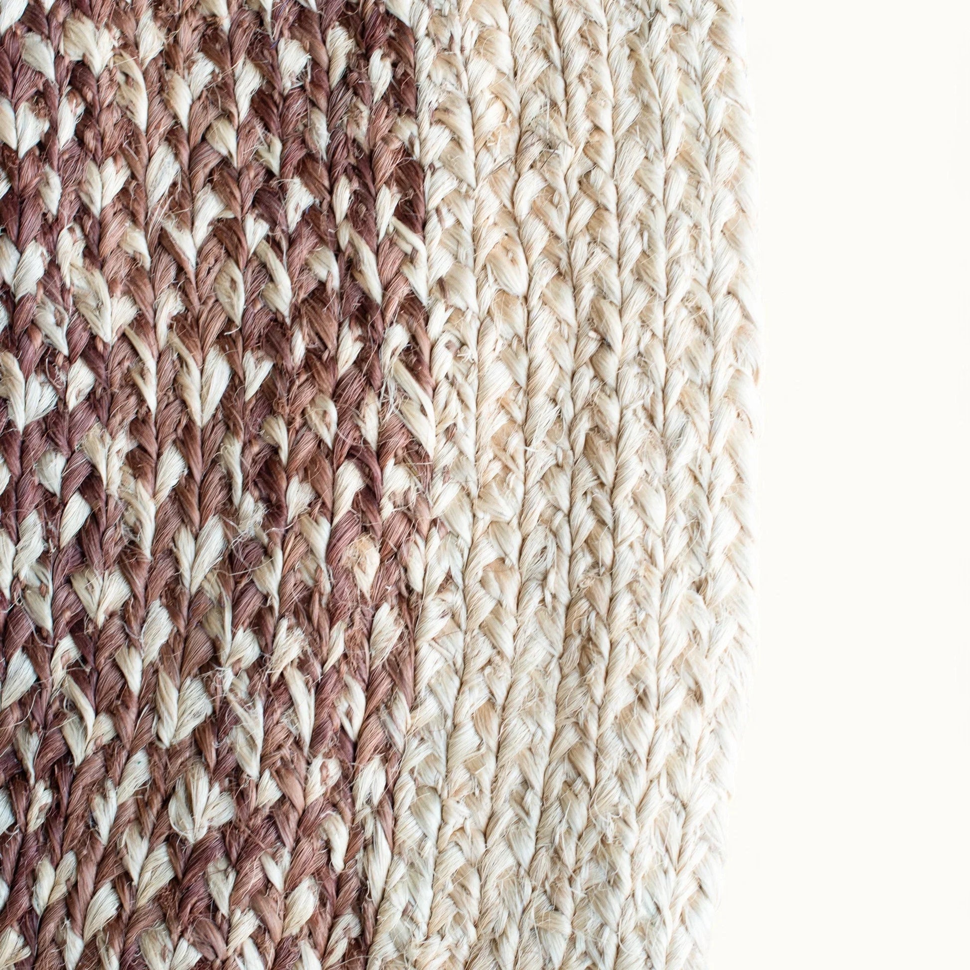 Close-up fiber detail of medium round sisal rug red earth variant showing two-tone braid transition between muted rose brown and natural cream sisal fiber bundles on white background