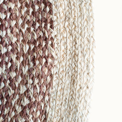 Close-up fiber detail of medium round sisal rug red earth variant showing two-tone braid transition between muted rose brown and natural cream sisal fiber bundles on white background