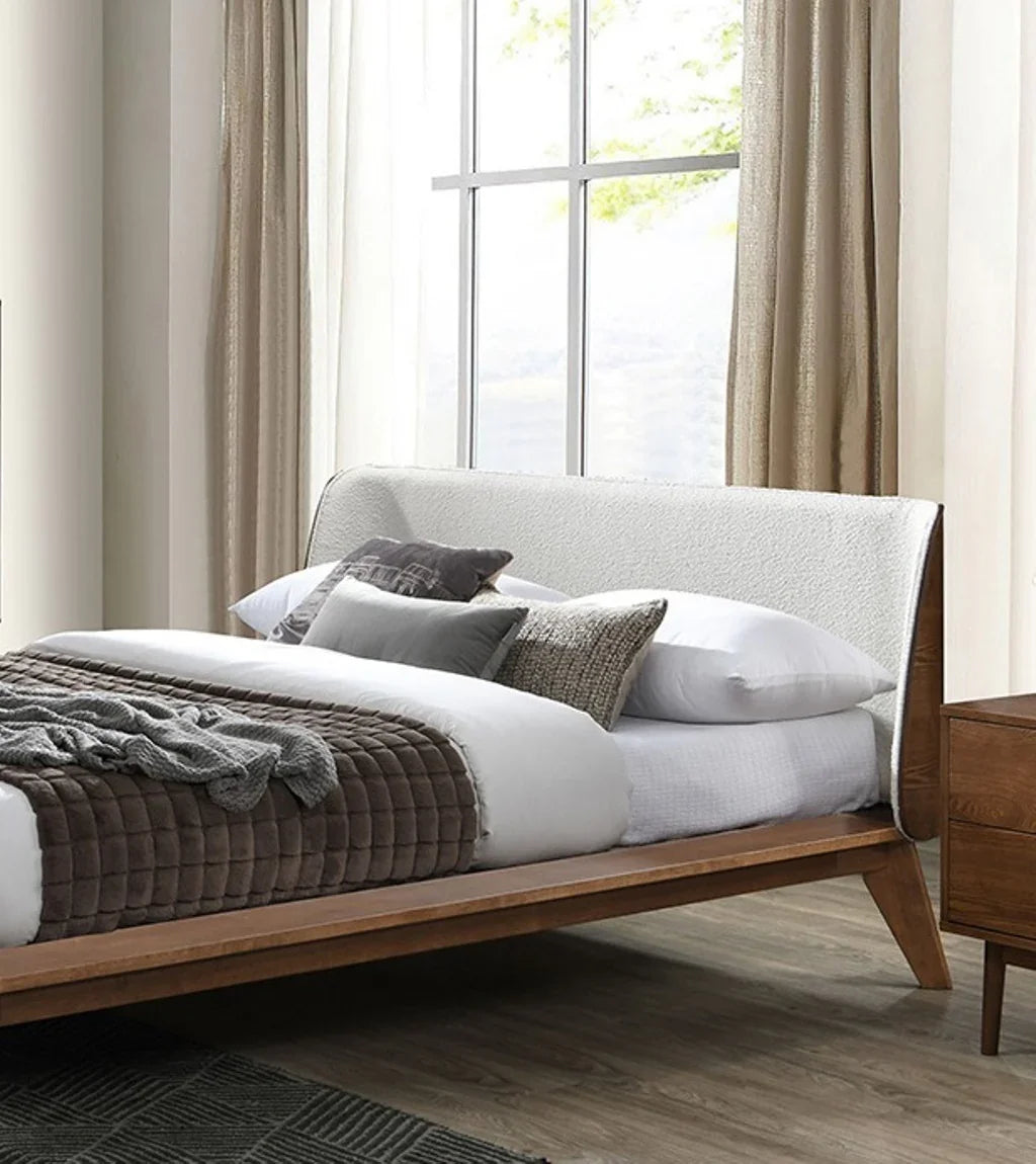 ​Close-up view of a mid century full bed panel headboard upholstered in tactile beige boucle fabric with sleek winged edges and accent pillows