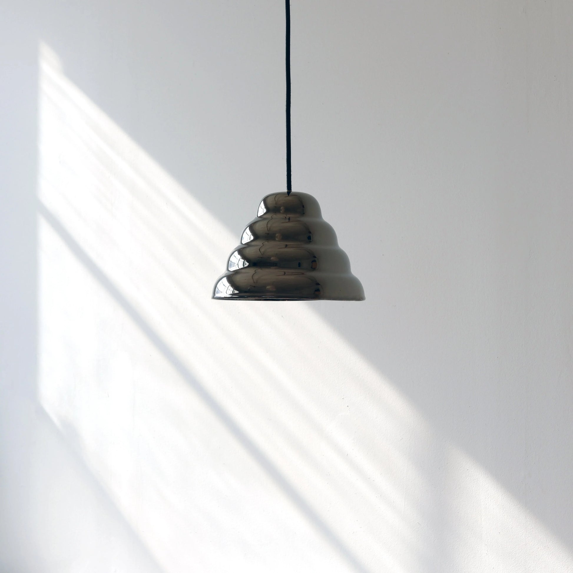 Modern ceramic pendant light casting architectural shadows on a clean minimalist white wall with natural sunlight streaming across the surface