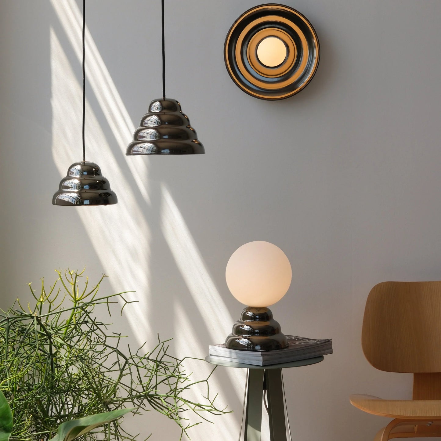 Modern ceramic pendant lights hanging beside a matching concentric wall sconce and a glass globe table lamp on a minimalist side table near a wood accent chair